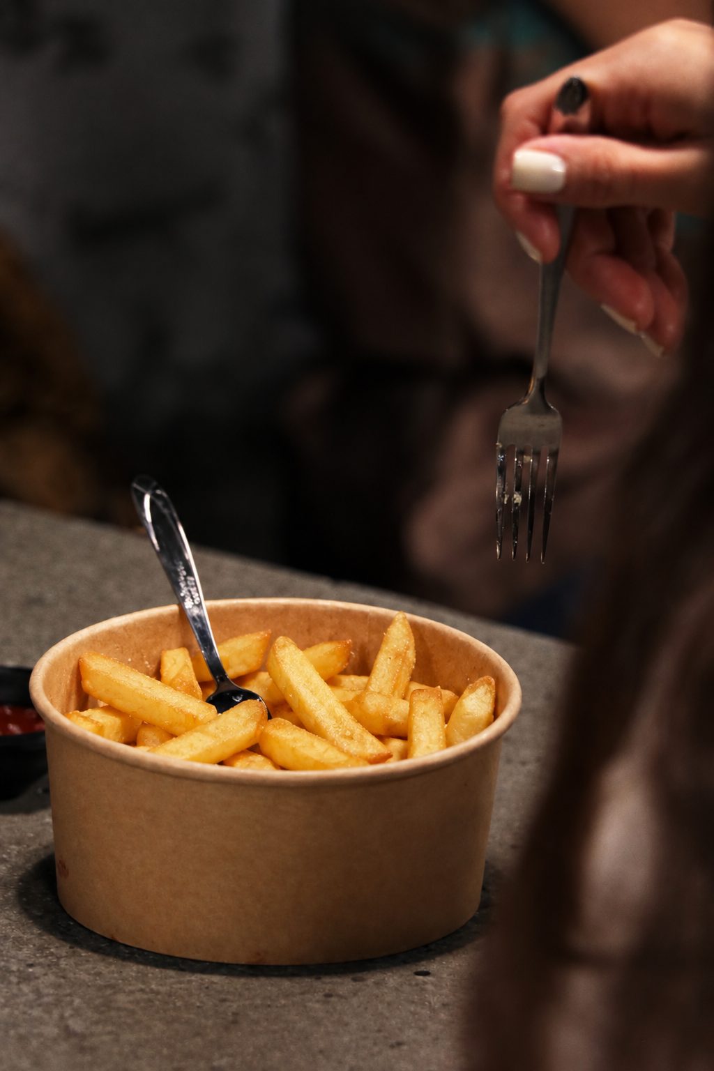 A cup of fries being eaten with a fork